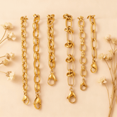 The Amalfi Layering Set by Luminova: all six waterproof gold chain bracelets laid out vertically, showcasing each unique style on a soft beige background with dried flowers.