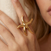 Close up of woman wearing chunky gold starfish ring statement jewelry on middle finger.