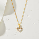 A detailed studio shot of The Devotion Necklace by Luminova, showcasing the sparkling crystal pavé open heart pendant on a gold chain, styled on a white background with water droplets.