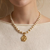 Close up of woman wearing gold beaded pearl necklace with organic coin pendant on collarbone.
