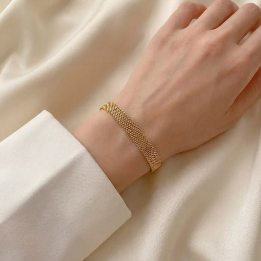 Close up of woman's wrist wearing gold mesh chain bracelet soft woven texture.