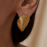 Close up detail of textured gold mussel shell earring on model ear.
