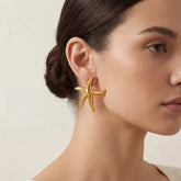 Close up of woman wearing chunky gold starfish statement earring mermaidcore style.