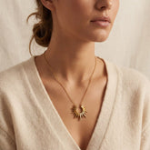 Close up of woman wearing Helios gold sunburst necklace with beige cardigan everyday style.