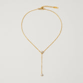 A detailed studio shot of The Reine Necklace by Luminova, showcasing the delicate gold Y-necklace with its sparkling crystal crown and single crystal drop.