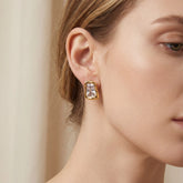 Close up of woman wearing gold signet style stud earrings with clear rectangular crystal.