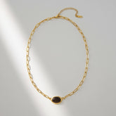 A detailed studio shot of The Terra Necklace by Luminova, showcasing the minimalist gold paperclip chain with a single, oval-cut Tiger Eye stone pendant in soft lighting.