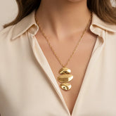 A beautiful close-up of The Thalia Necklace on a model's collarbone, highlighting the bold, artistic statement of the cascading gold pendant.