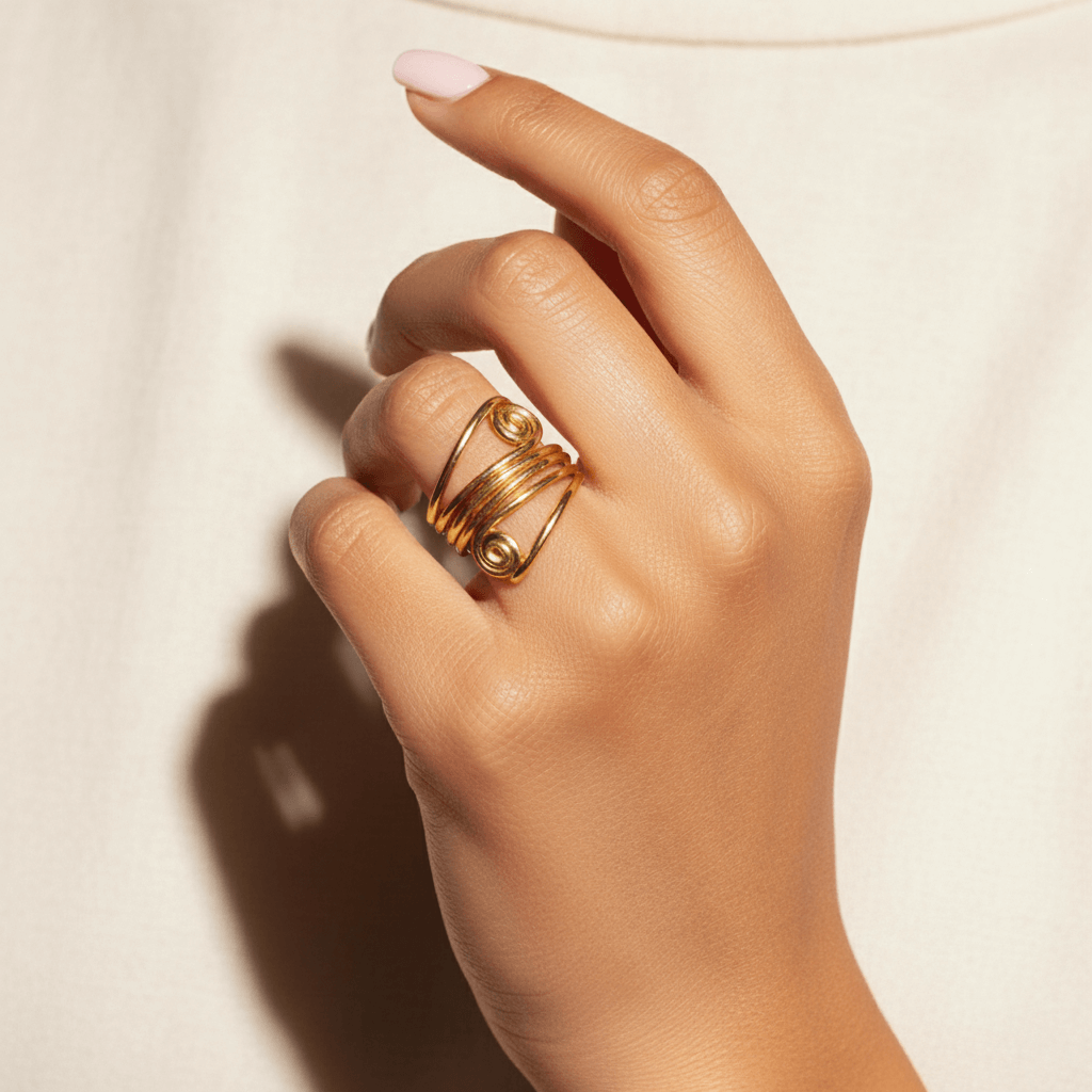 A model's hand with neutral-toned nails, showcasing The Oracle Ring worn on her index finger. The ring's wide, multi-layered band and bold spiral design create a powerful, armor-like statement.
