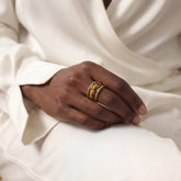 Black woman wearing gold tiger's eye stacking ring on white outfit elegant style.