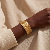 Dark skin model wearing wide liquid gold textured cuff bracelet vintage style.