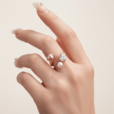 A close-up of a model's hand with a fresh, nude manicure, wearing The Celestial Ring in gold on her ring finger. The ring's open cuff design and the cluster of the crystal and pearls are beautifully showcased.
