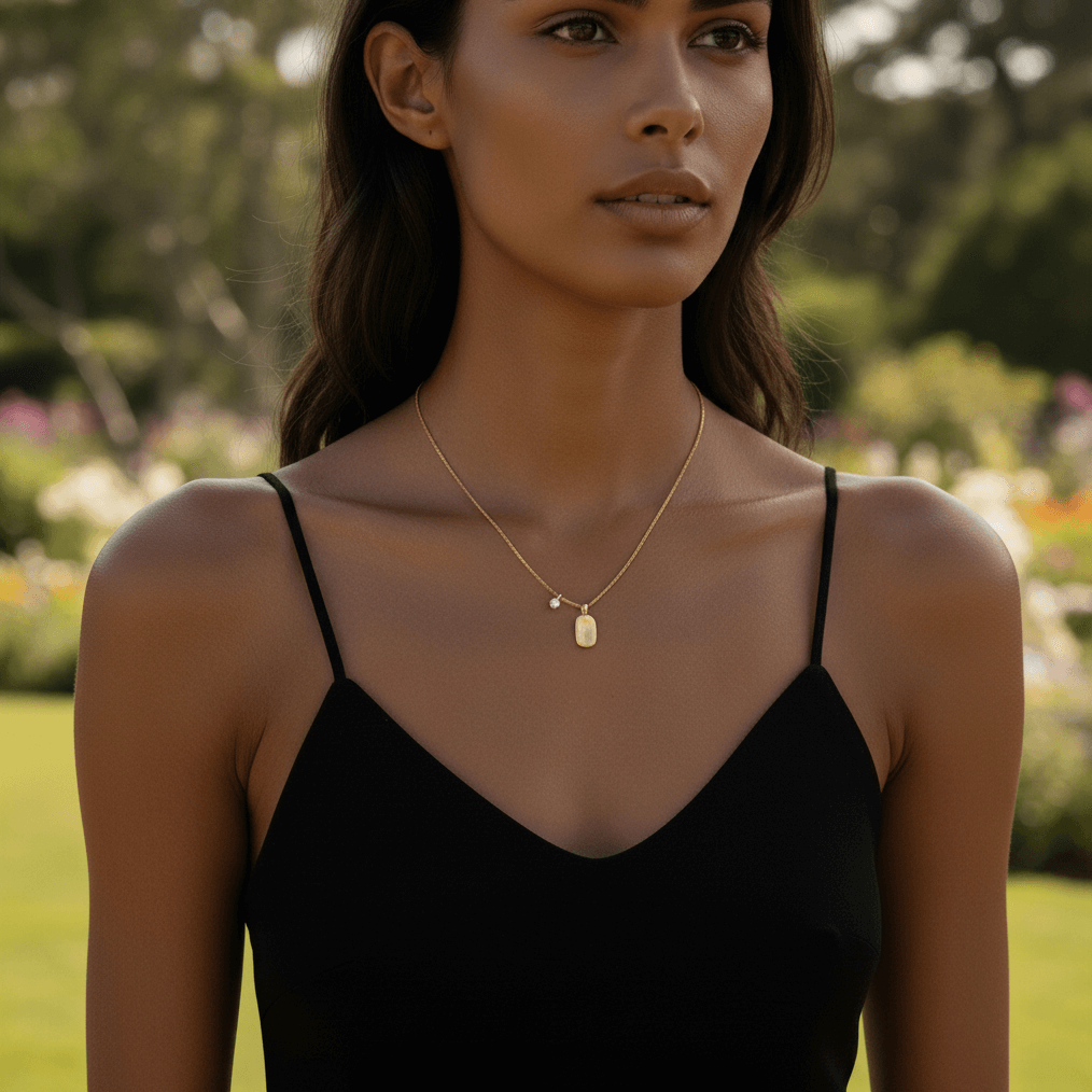 A model wearing a soft, beige cashmere sweater, with the delicate gold Signature Necklace visible at her neckline. The warm, matte finish of the pendant complements the cozy texture of the sweater, creating a look of understated, everyday luxury