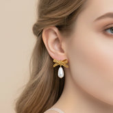 A close-up side profile of a model wearing The Clara Earrings, showcasing the delicate pearl drop and how the elegant gold bow sits on the earlobe.