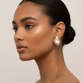 Side profile of a model with glowing skin wearing The Theia Earrings, highlighting their bold scale and how the organic gold setting curves around the earlobe.