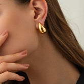 A close-up of a model wearing the gold Ambrosia Studs, highlighting how the elegant, puffy teardrop design curves up the earlobe for a modern look.