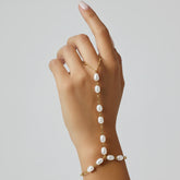 A model's hand with her finger raised, showing the delicate fit of the pearl finger loop on The Nereid Hand Chain.