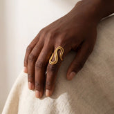 Dark skin model styling gold sculptural drift ring on index finger modern jewelry.