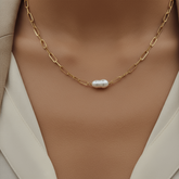 A super close-up shot of The Aphrodite Necklace on a woman's neck, highlighting the beautiful luster of the baroque pearl against the skin.