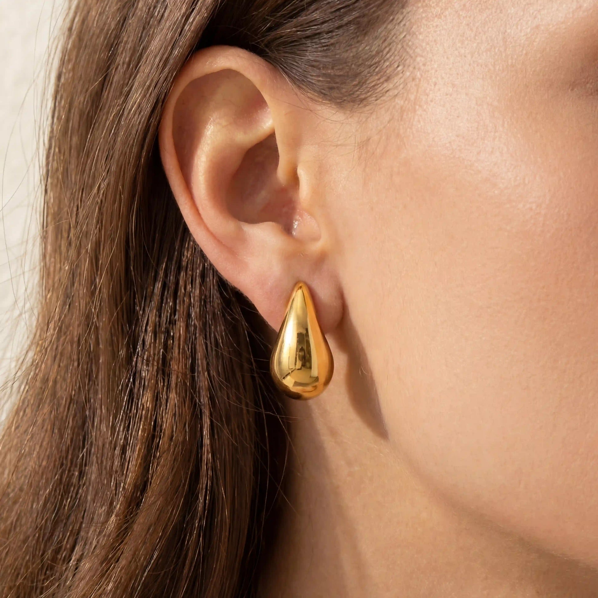 Close up of woman wearing gold Ambrosia teardrop stud earrings liquid metal design.