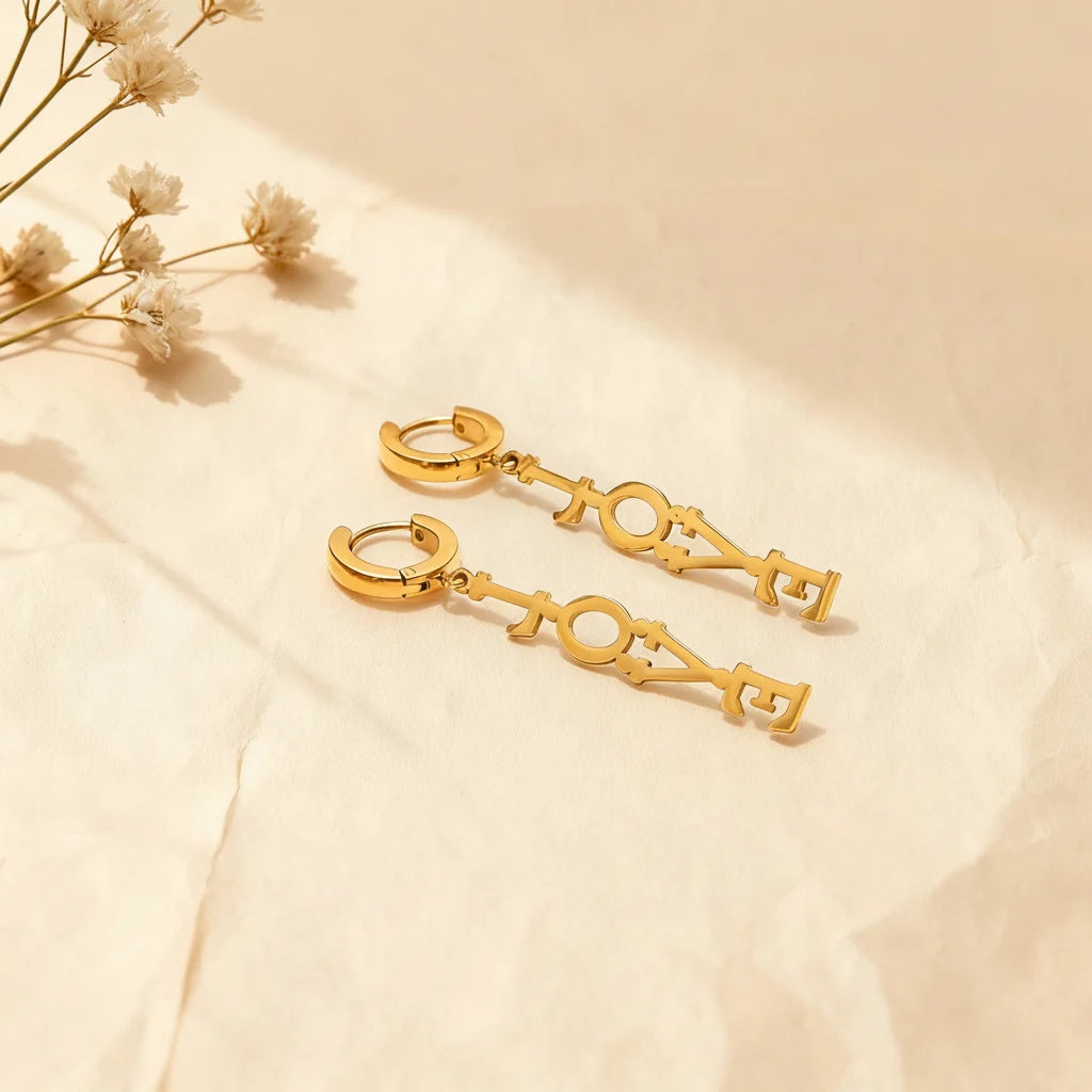 An artistic shot showing the detachable 'LOVE' charm separated from the gold huggie hoop, illustrating the versatile design of The Amor Earrings.