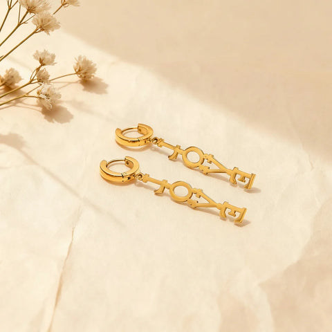 An artistic shot showing the detachable 'LOVE' charm separated from the gold huggie hoop, illustrating the versatile design of The Amor Earrings.