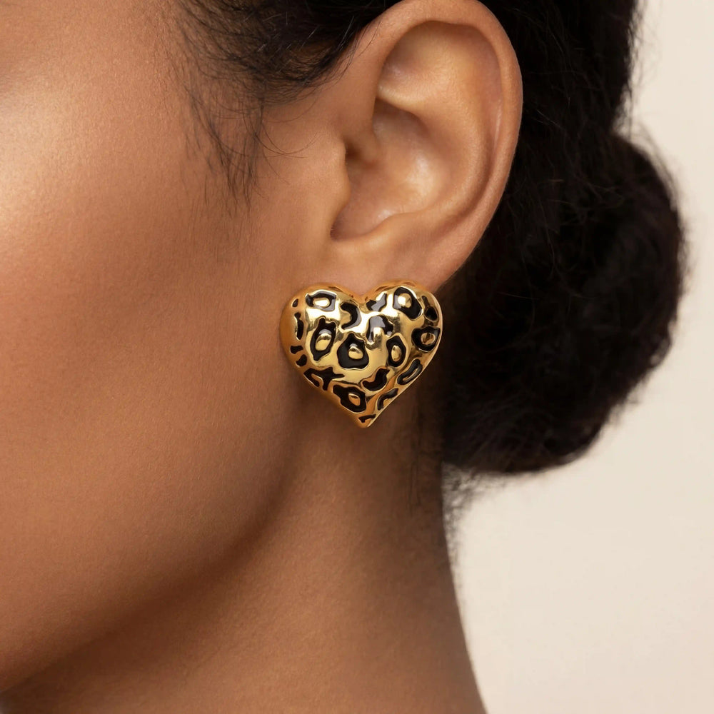 Close up of woman wearing large gold heart stud earrings with black leopard print pattern.