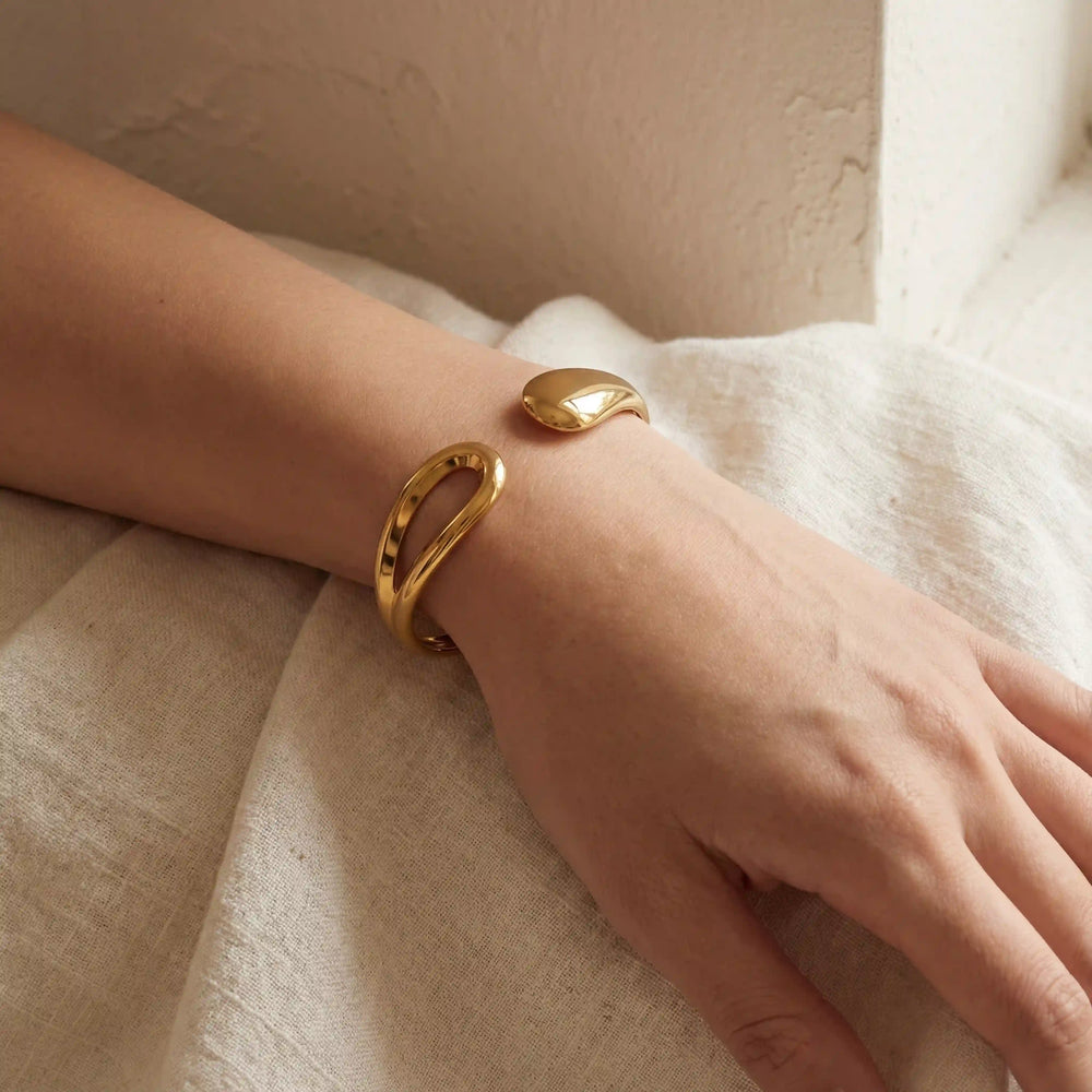 Woman wearing minimalist gold teardrop bangle on wrist cozy aesthetic.