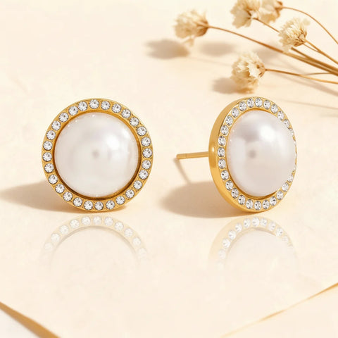 A detailed studio shot of The Athena Studs by Luminova, showing the classic round pearl and crystal halo earrings with their elegant reflection on a soft, warm background.