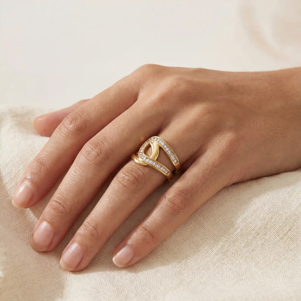 Close up of woman wearing gold crossover ring with baguette crystals on ring finger.