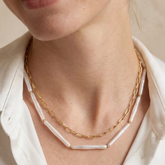 Close up of woman wearing Callisto layered necklace featuring gold paperclip chain and white tube beads.