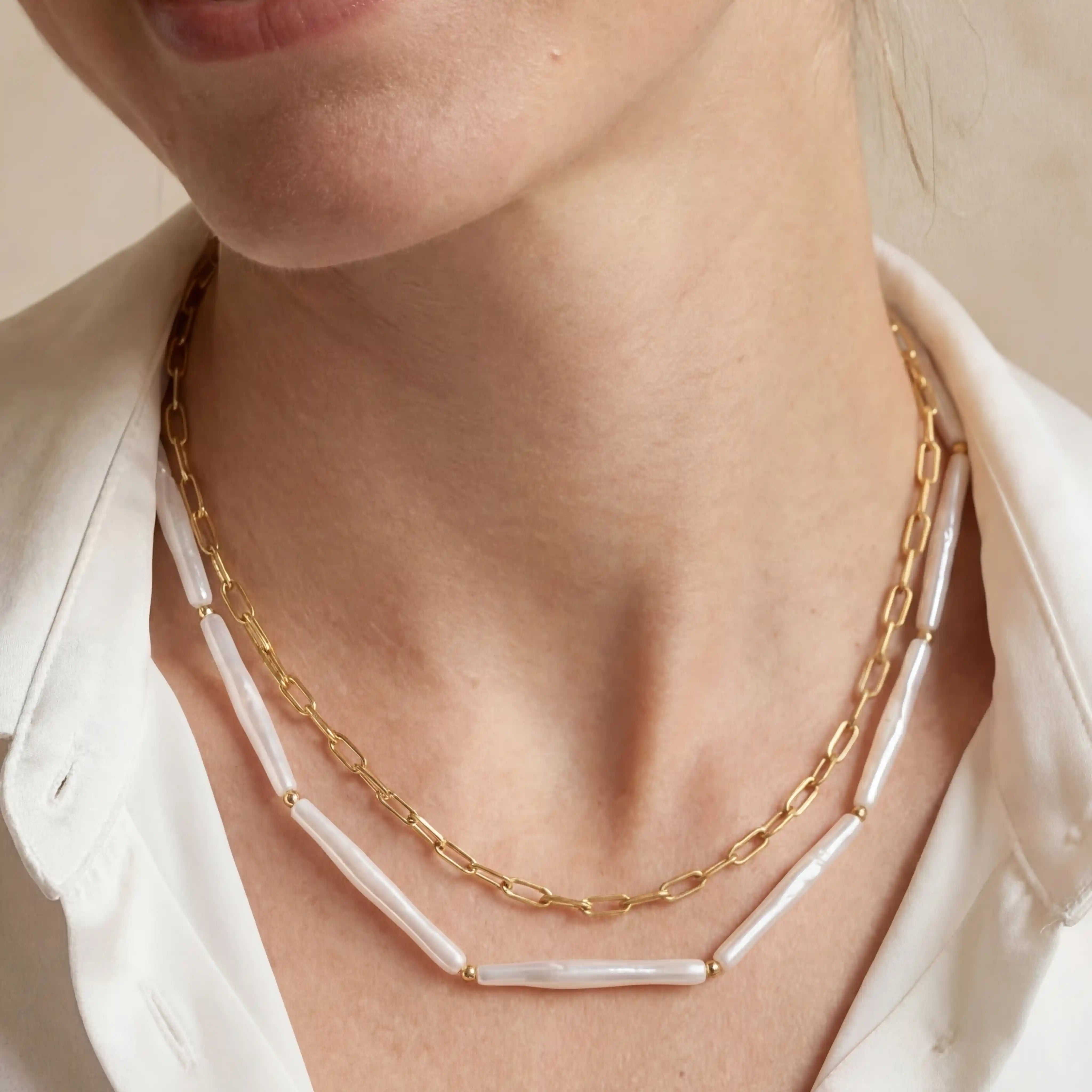 Close up of woman wearing Callisto layered necklace featuring gold paperclip chain and white tube beads. Main image