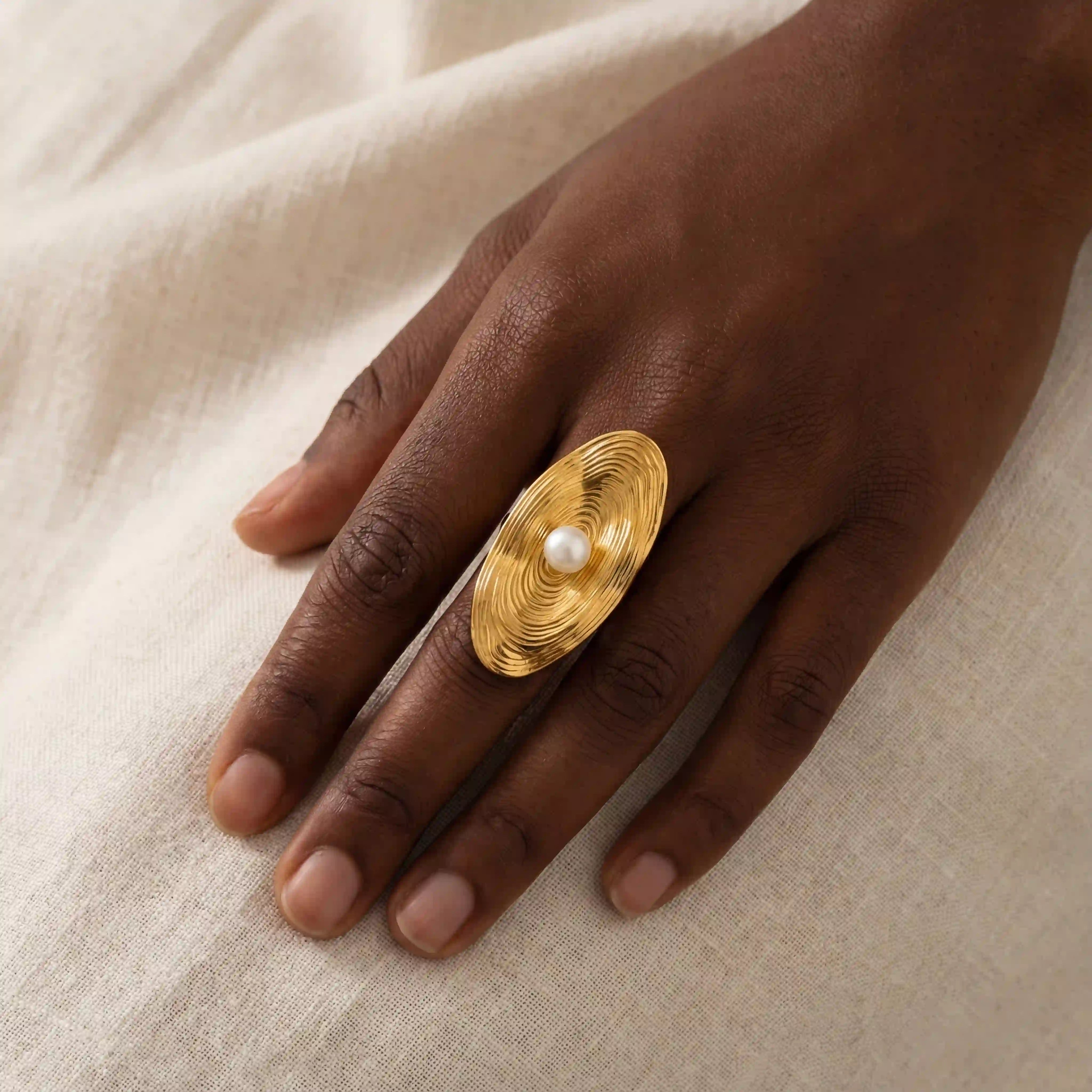 Dark skin model styling Calypso gold statement ring with pearl on linen background. Main image