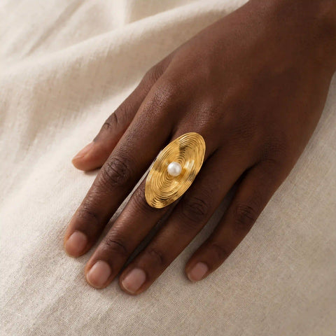 Dark skin model styling Calypso gold statement ring with pearl on linen background.
