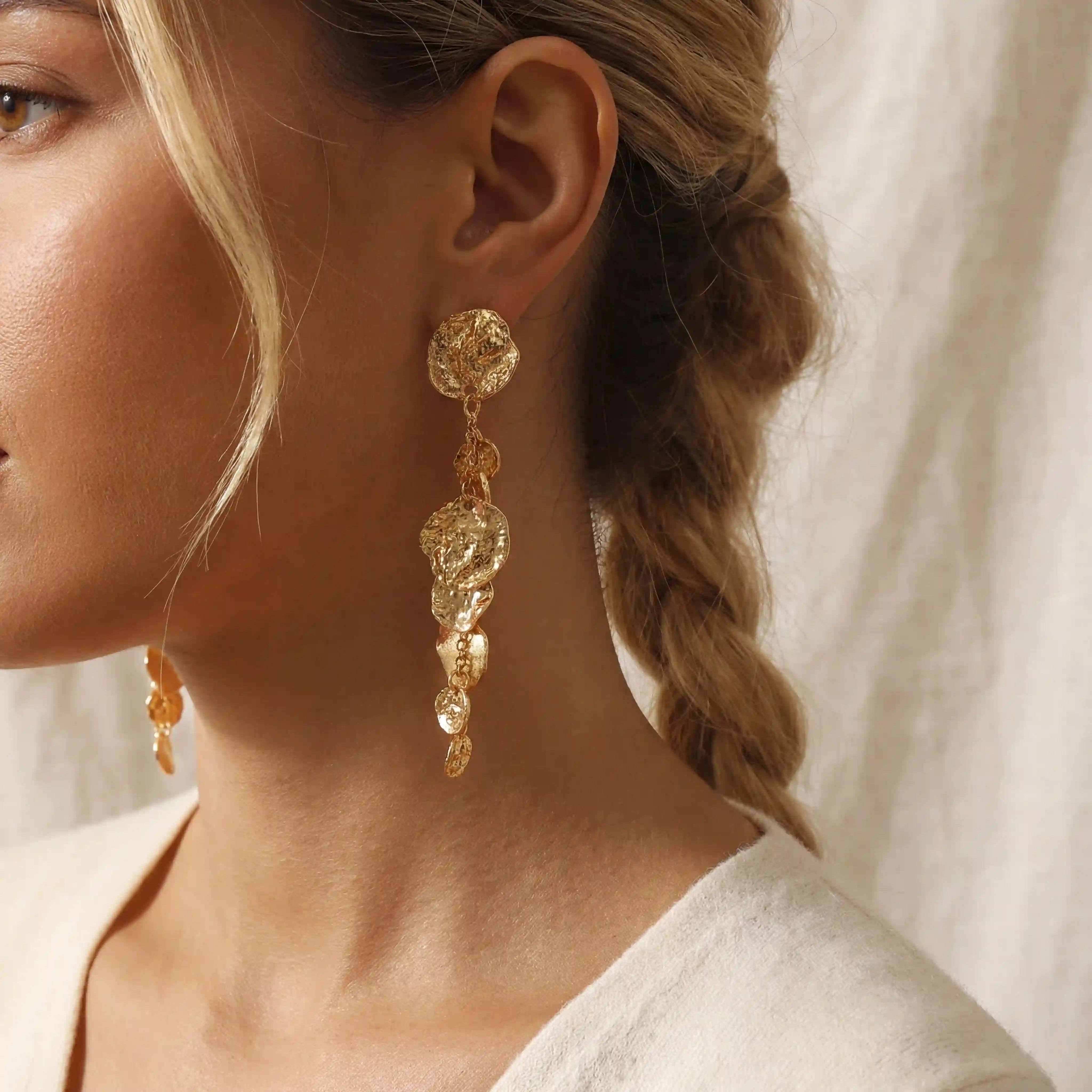 Close up side view of blonde woman wearing long gold hammered coin earrings bohemian style.