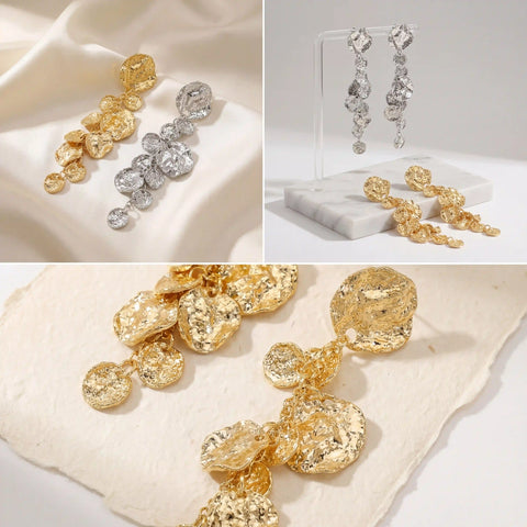 Aesthetic flat lay of long gold and silver textured earrings on beige stone background.