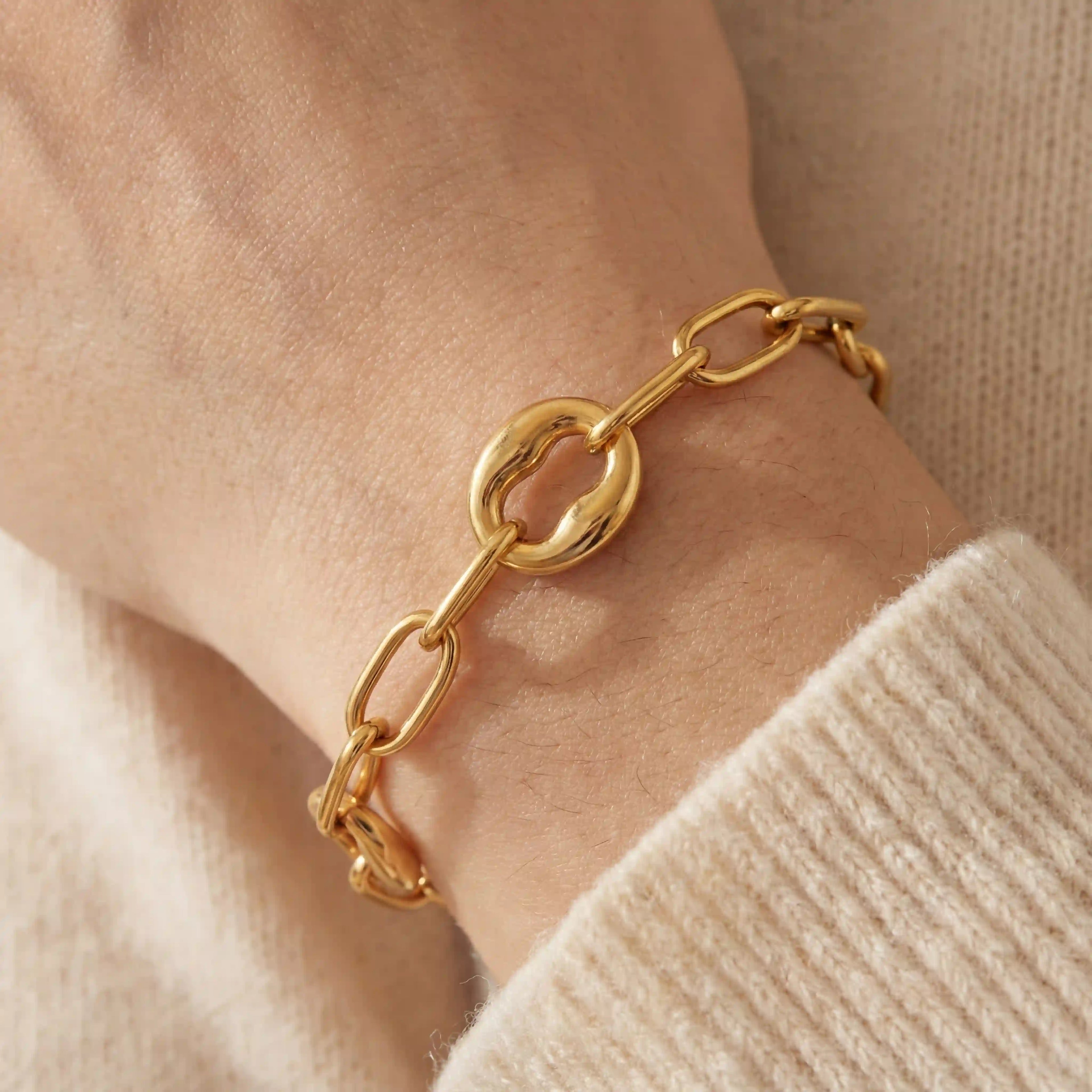 Close up of woman wearing chunky gold link bracelet with alternating organic oval links.