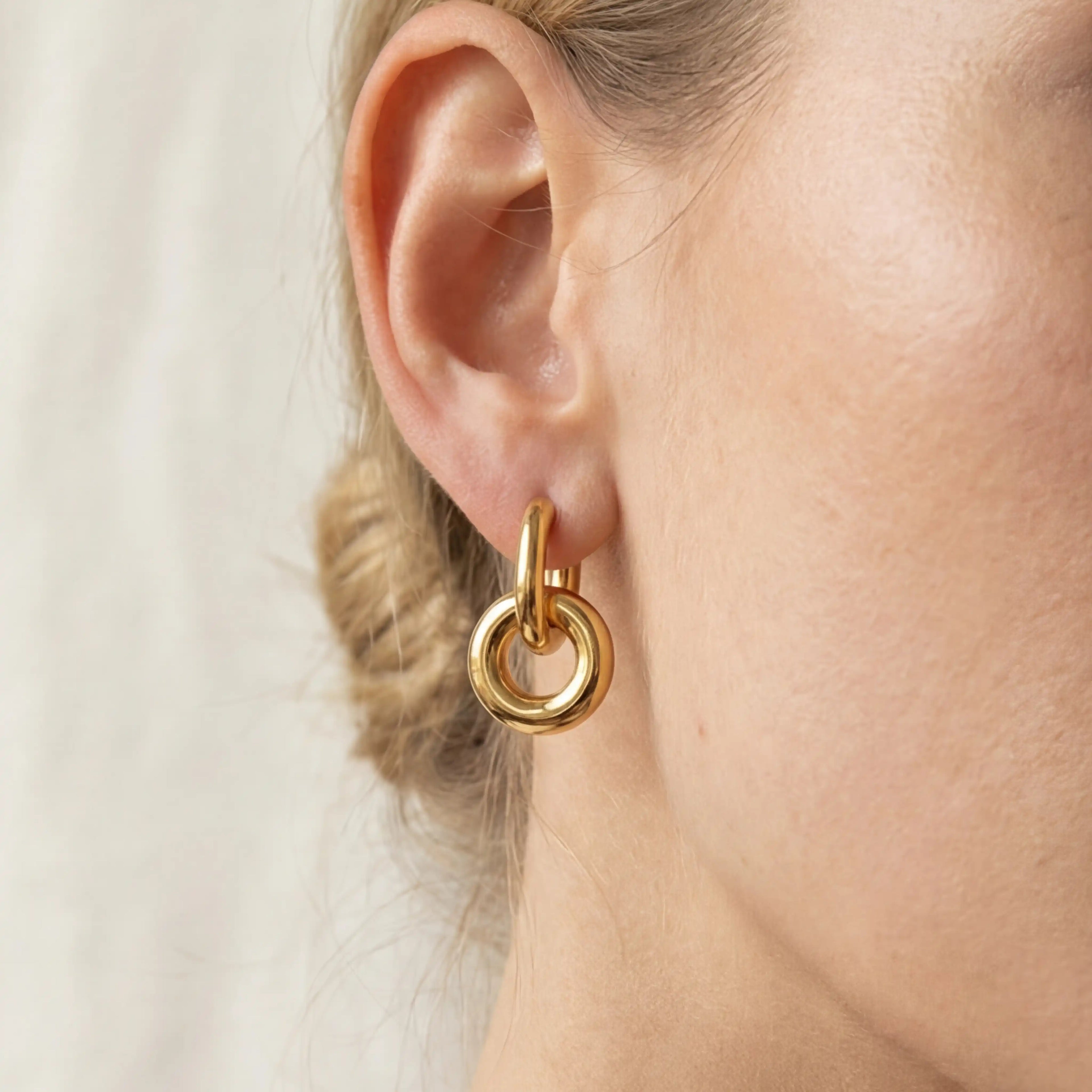 Close up of woman wearing chunky gold twist knot hoop earrings interlocking design.
