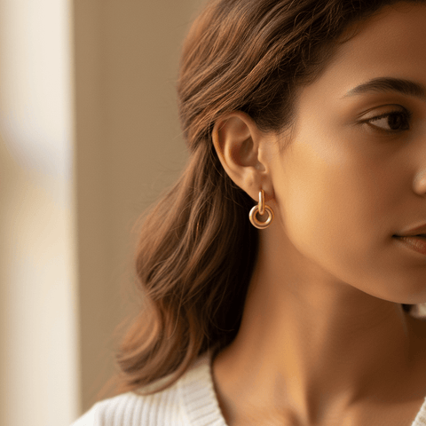 Close-up side profile of a woman wearing Luminova gold knot hoops, showcasing how they dangle from the ear.