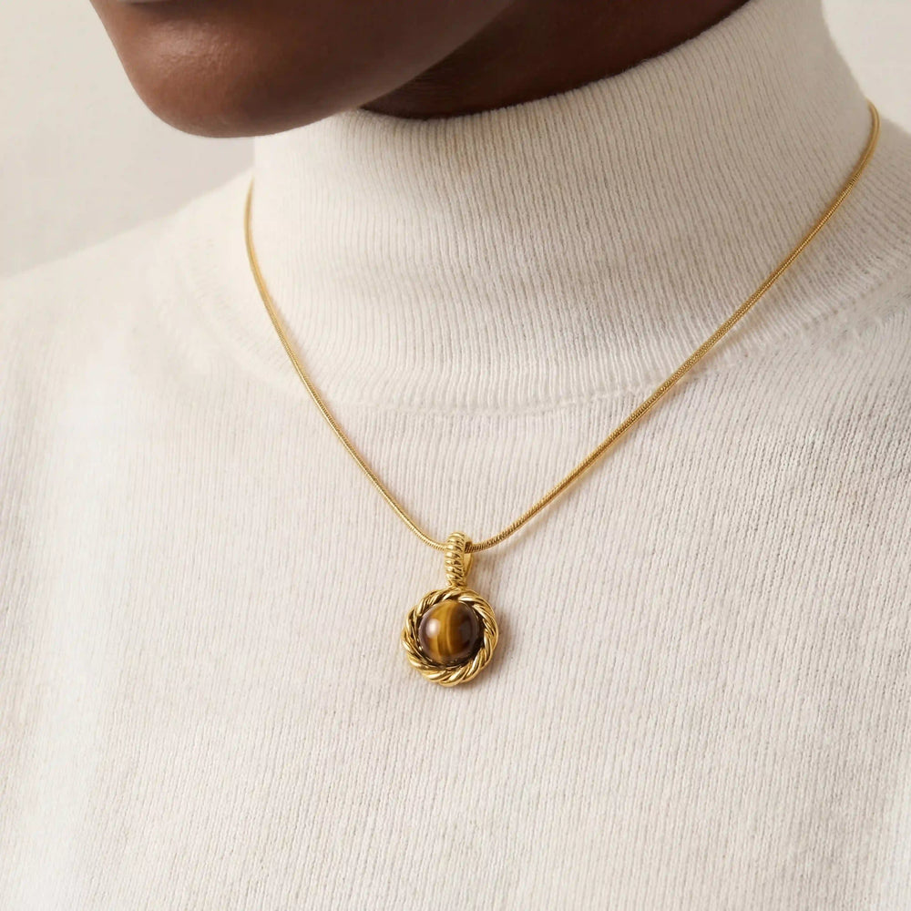 Close up of gold snake chain necklace with round tiger's eye stone pendant on woman.