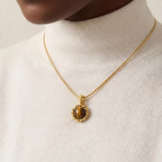 Close up of gold snake chain necklace with round tiger's eye stone pendant on woman.