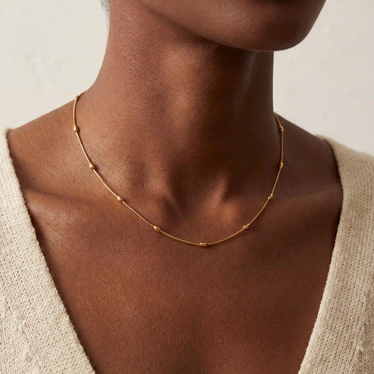 Close up of woman with dark skin wearing dainty gold beaded satellite chain necklace.