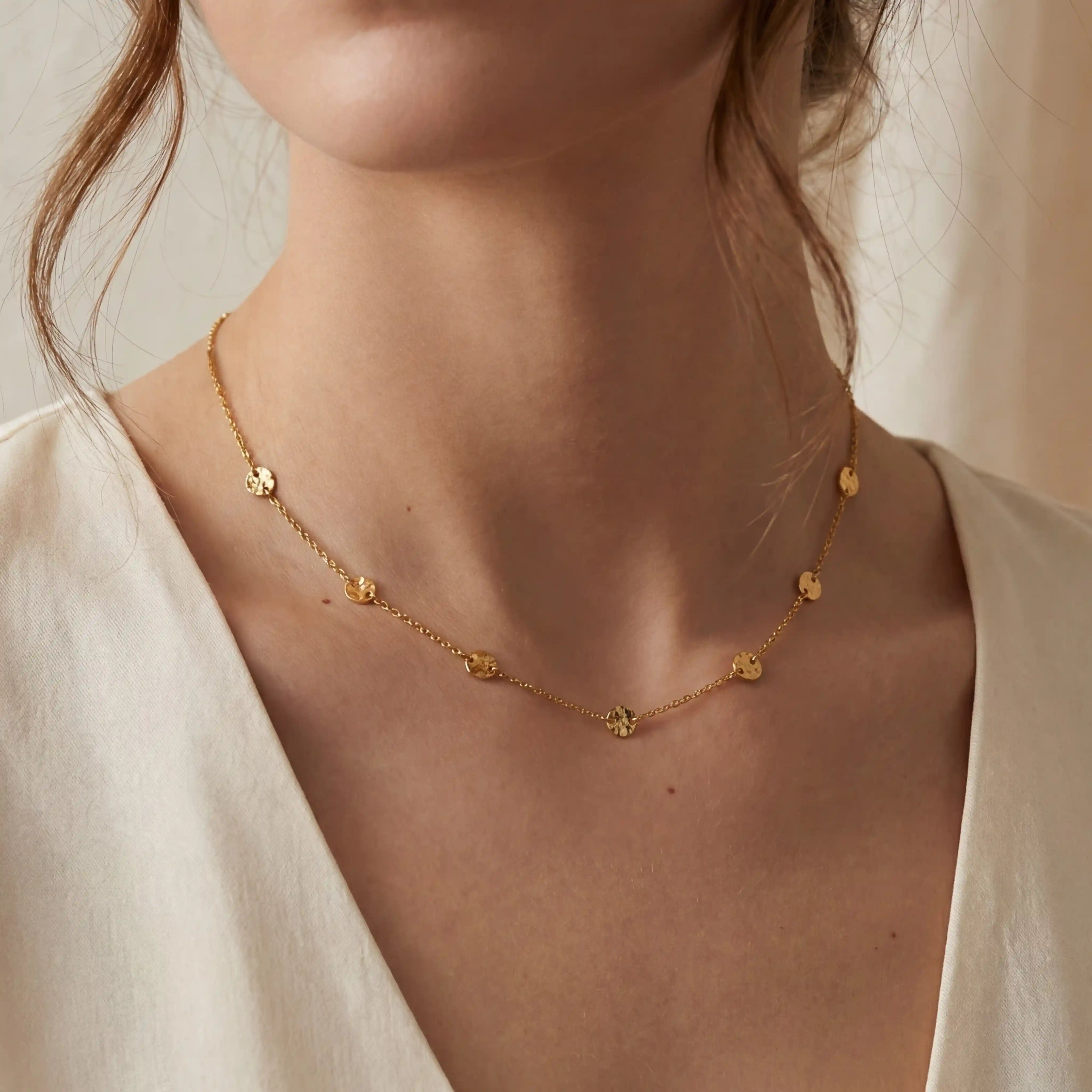 Close up of woman wearing dainty gold station necklace with bezel set crystals on collarbone. Main image
