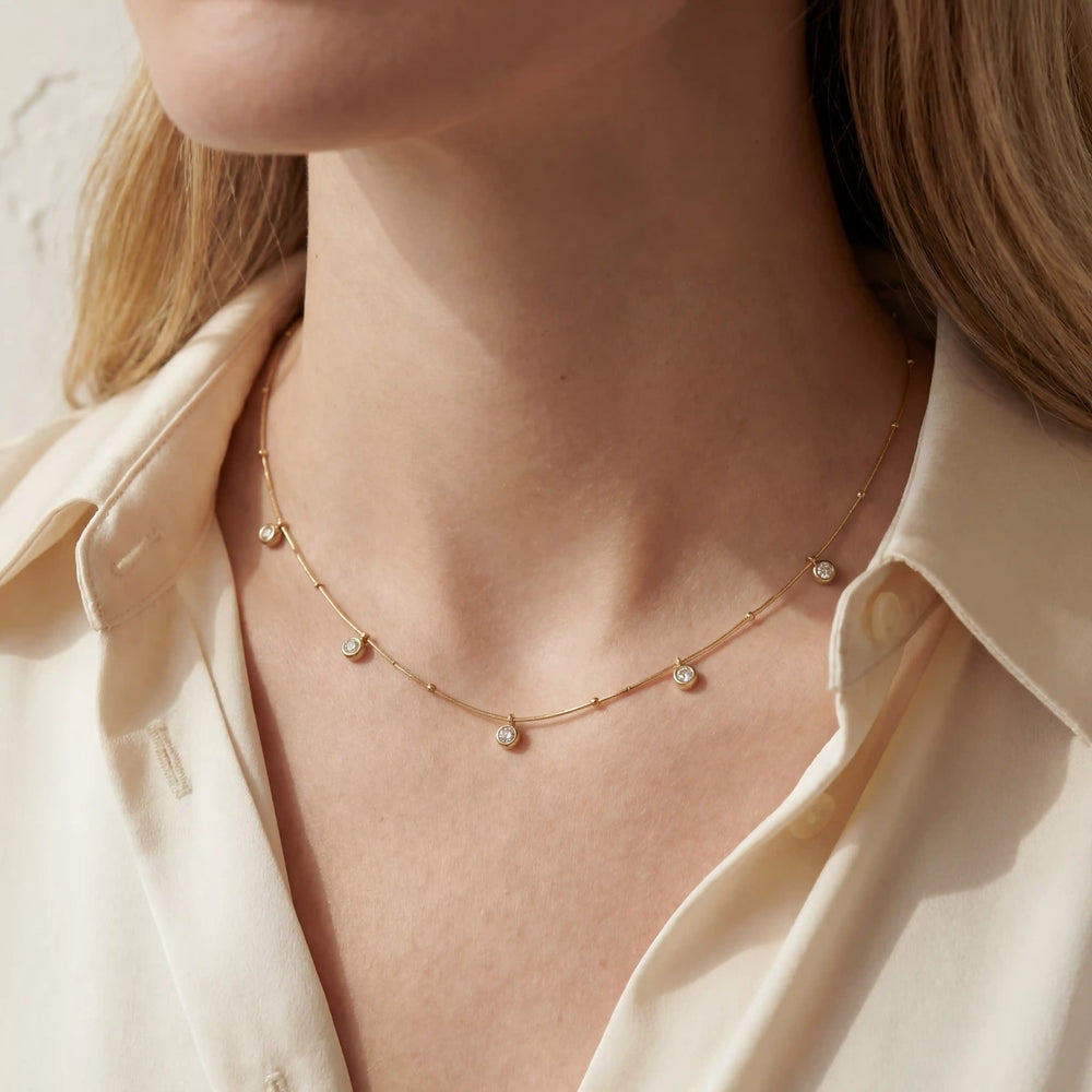 Close up of woman wearing dainty gold drop station necklace on collarbone minimalist style.
