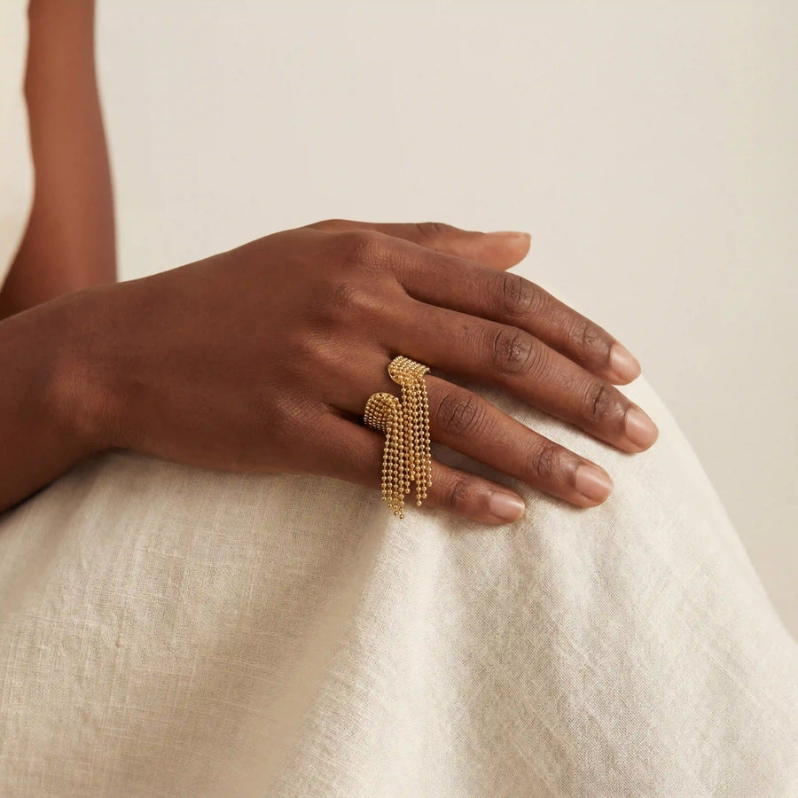 Dark skin model wearing Danaë gold fringe ring with cascading chain tassel design.