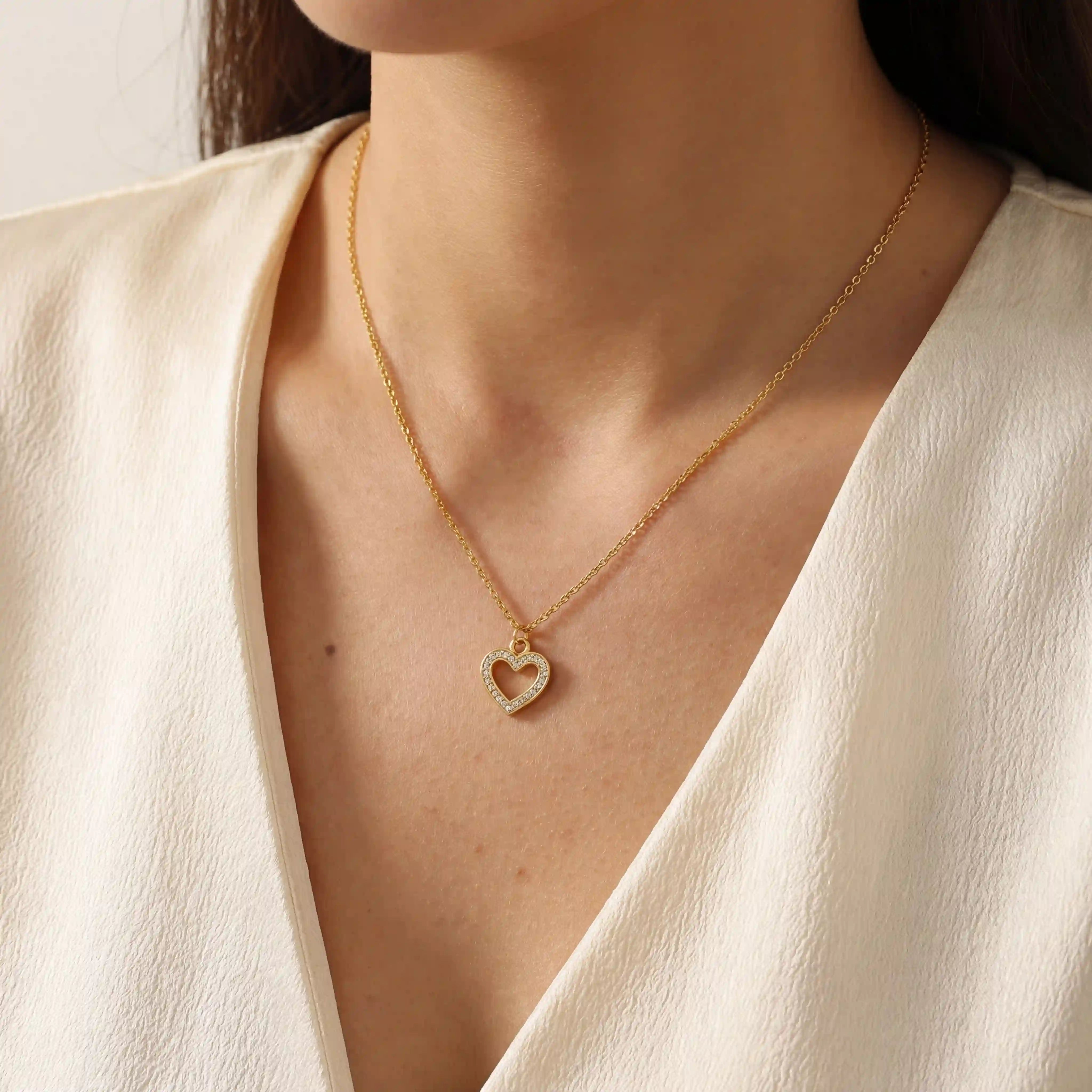 Close up of woman wearing gold Devotion necklace with crystal heart pendant on v-neck top. Main image