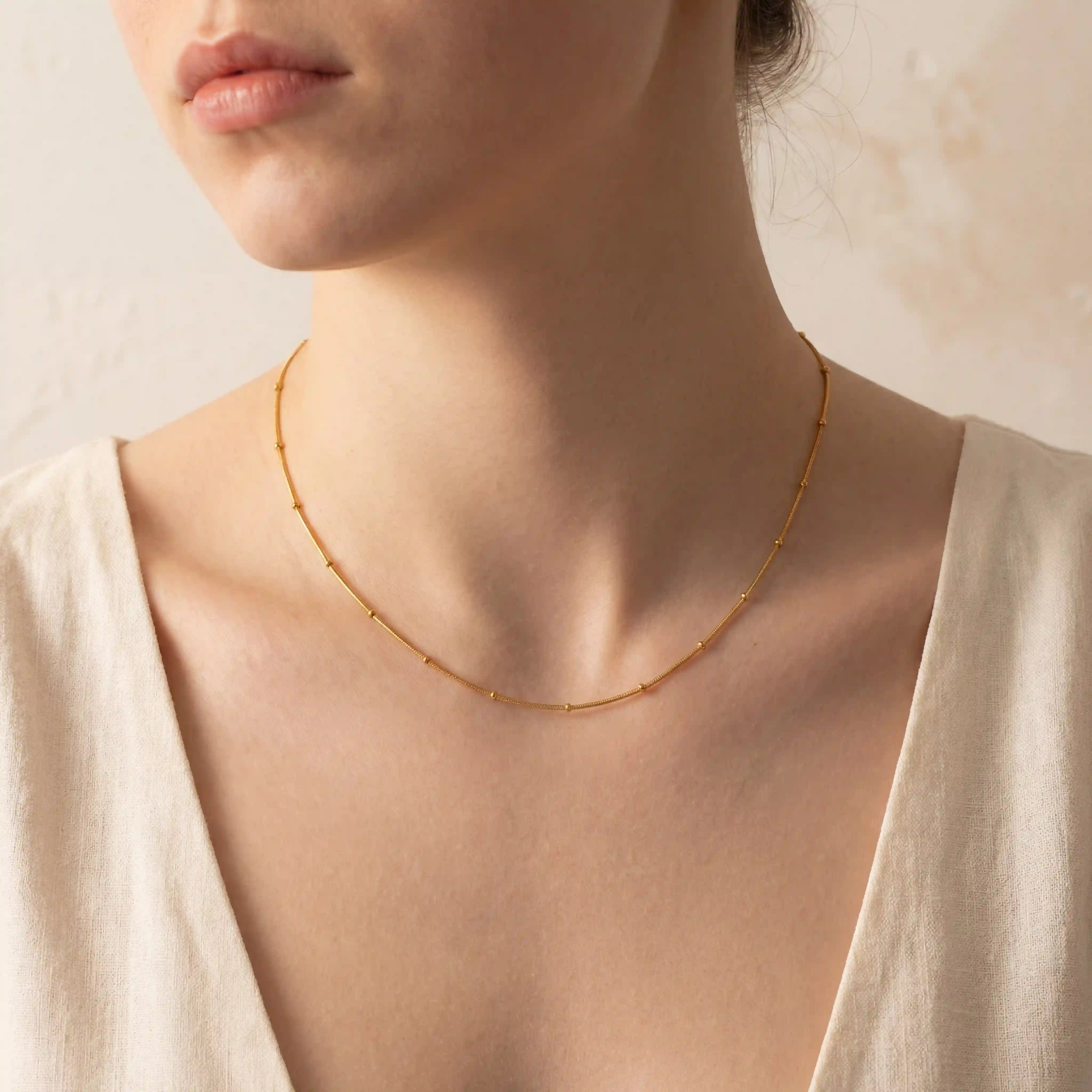 Close up of woman wearing gold dotted bead chain necklace minimalist collarbone jewelry.