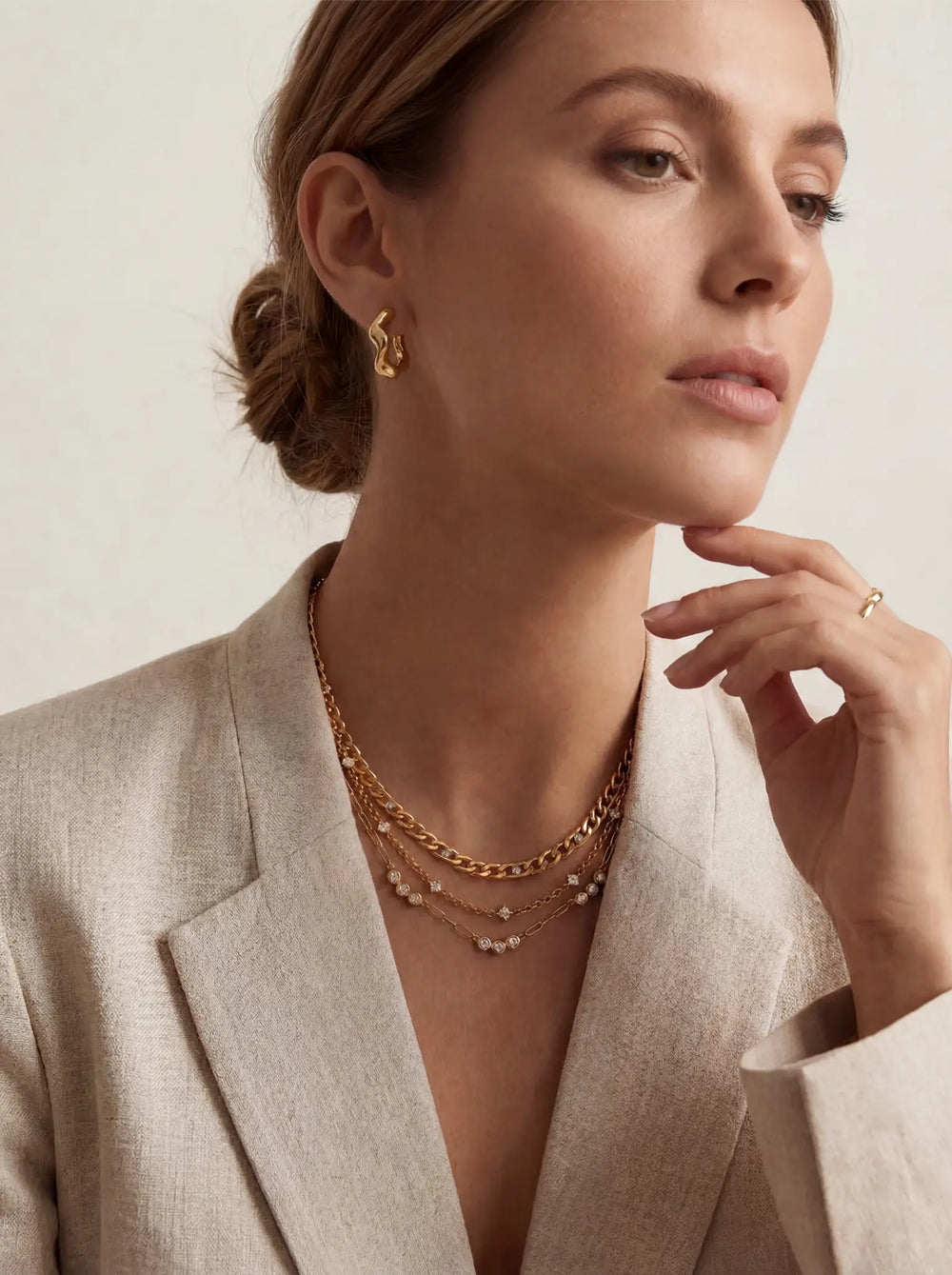 Lifestyle photography of blonde woman styling gold crystal station necklace layered with blazer office chic.
