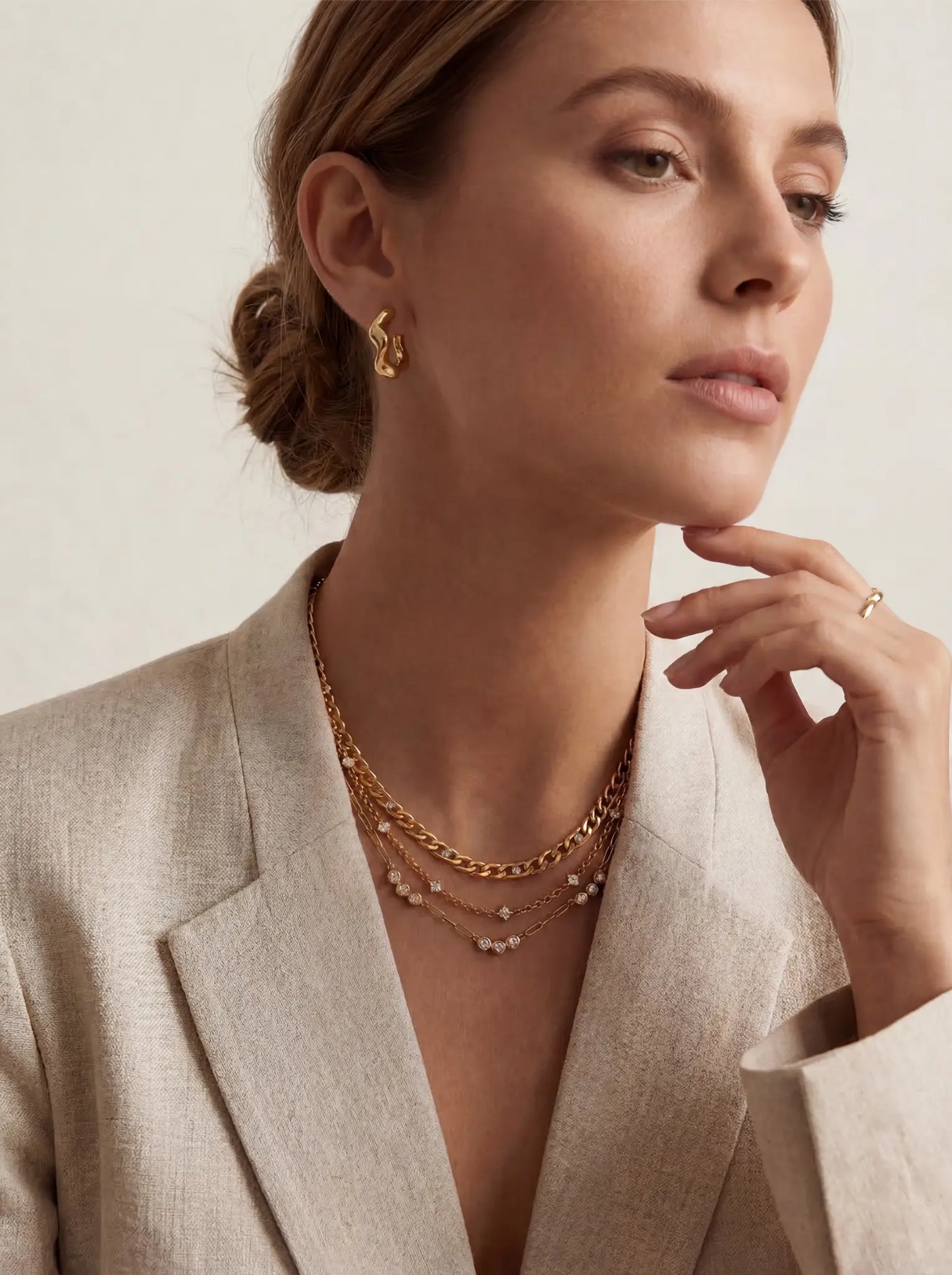 Lifestyle photography of blonde woman styling gold crystal station necklace layered with blazer office chic.