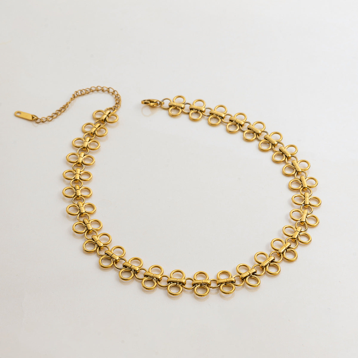 A detailed studio shot of The Elodie Choker by Luminova, laid out in a circle to showcase its delicate, continuous chain of minimalist gold clover links.